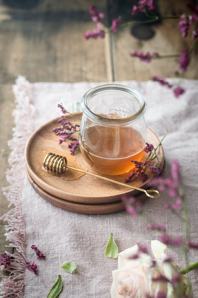 A rustic still life of a honey jar, gold dipper, and flowers on a wooden table.